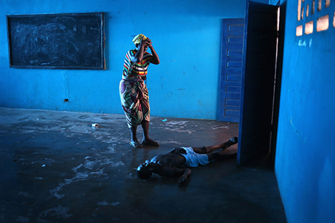 Umu Fambulle stands over her husband Ibrahim after he weakly got to his feet and fell, knocking him unconscious in an Ebola holding center on August 15, 2014 in the West Point township of Monrovia, Liberia. He died the same day. The Liberian capital was quickly overwhelmed by the epidemic in late summer, as the Ebola virus moved from a rural to an urban environment, making Monrovia the Ebola epicenter in West Africa. Only a decade after a long civil war, Liberia's fragile health system was unable to cope, international agencies were slow to react, and fear gripped the nation.